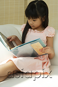AsiaPix - Little girl sitting on sofa reading book