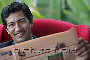 PictureIndia - Man reading financial newspaper, smiling at camera