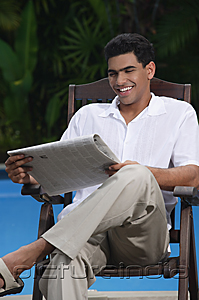 PictureIndia - Man sitting in chair by the pool, reading a newspaper