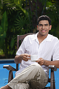 PictureIndia - Man sitting in chair by the pool, holding a cup and looking at camera