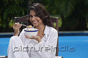PictureIndia - Woman in chair by the pool, holding bowl of cereal and looking at camera