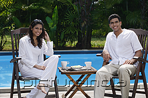 PictureIndia - Couple sitting by the pool, looking at camera