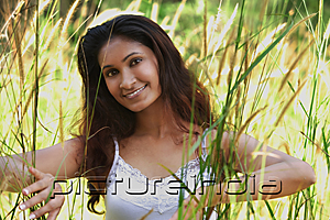 PictureIndia - Young woman in high grass smiling at camera