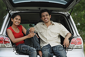 PictureIndia - Young couple sitting in car boot smiling at camera