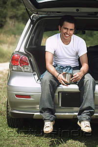PictureIndia - Young man sitting in car boot smiling at camera